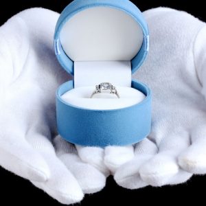 A picture of white gloves holding a ring with its box